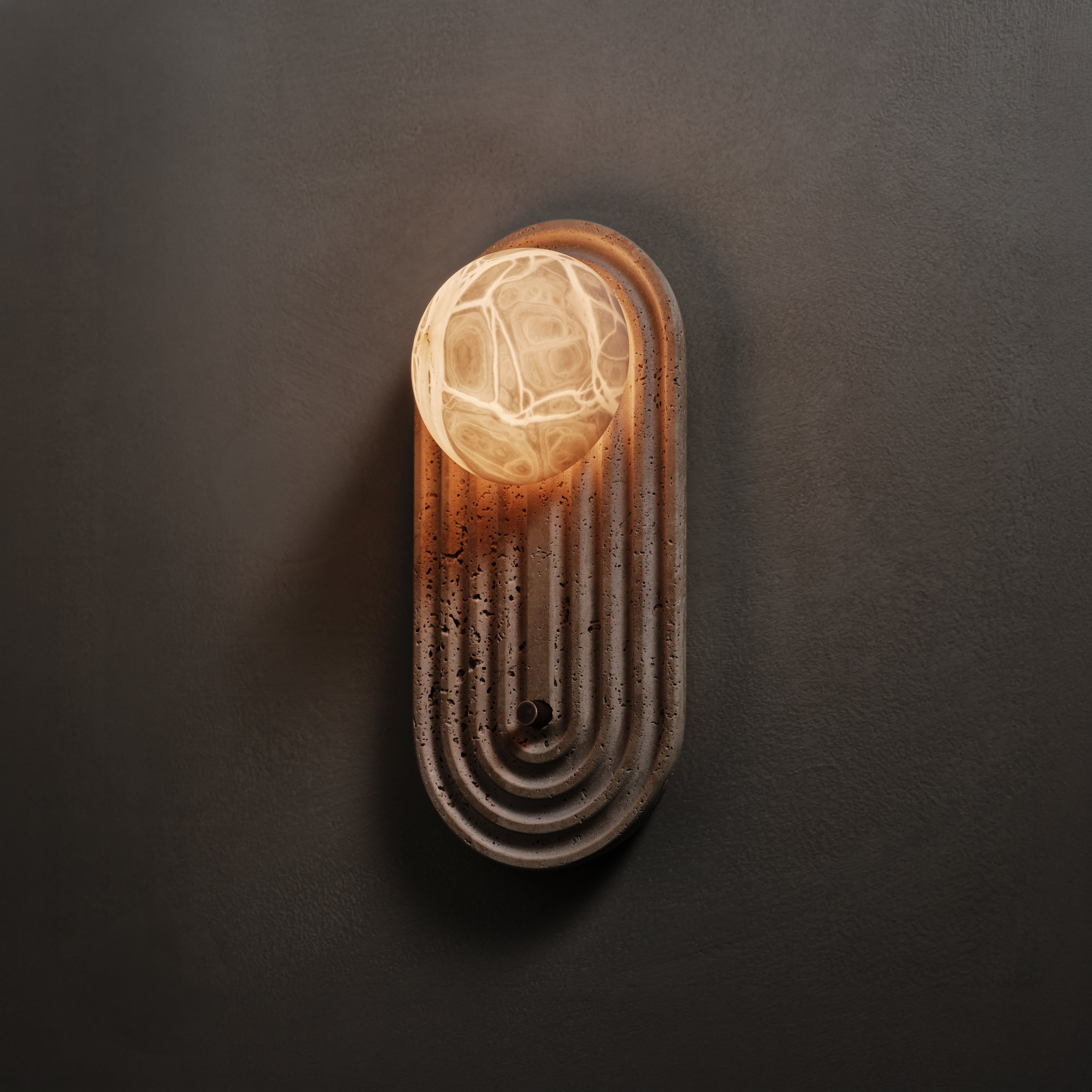 Sierra Wall Sconce in Travertine and brown wax polished, angled view, lit, Studio Baldo
